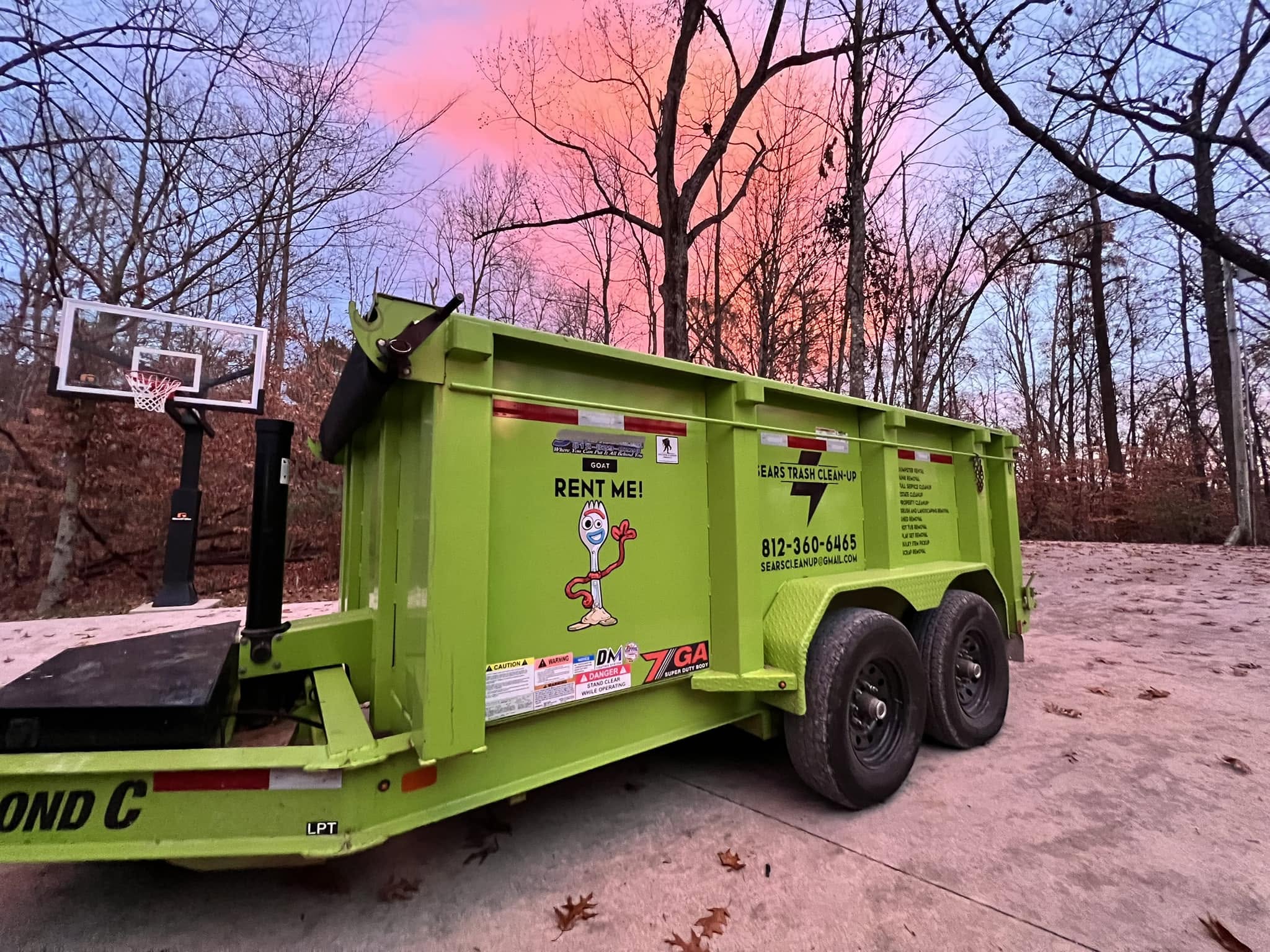 The Sears Trash Cleanup dumpster trailer beside a residential driveway at sunset